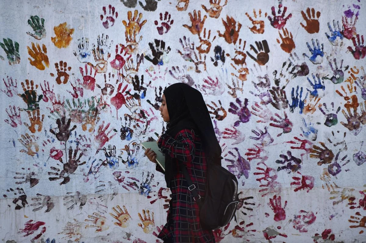 An Afghan girl walks past a handprint wall in Kabul, Afghanistan.