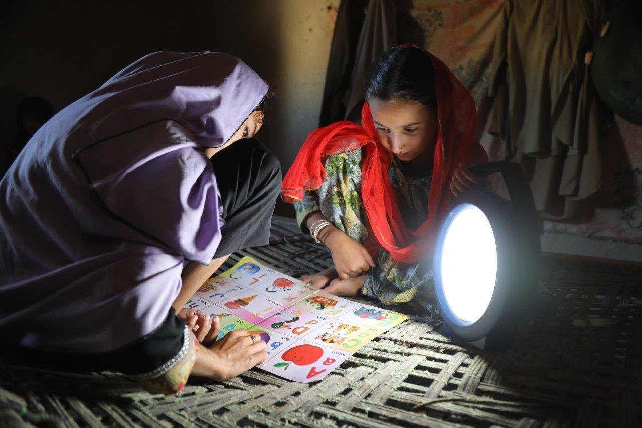 Two Afghan girls reading their school lessons in the shade of a lamp.
